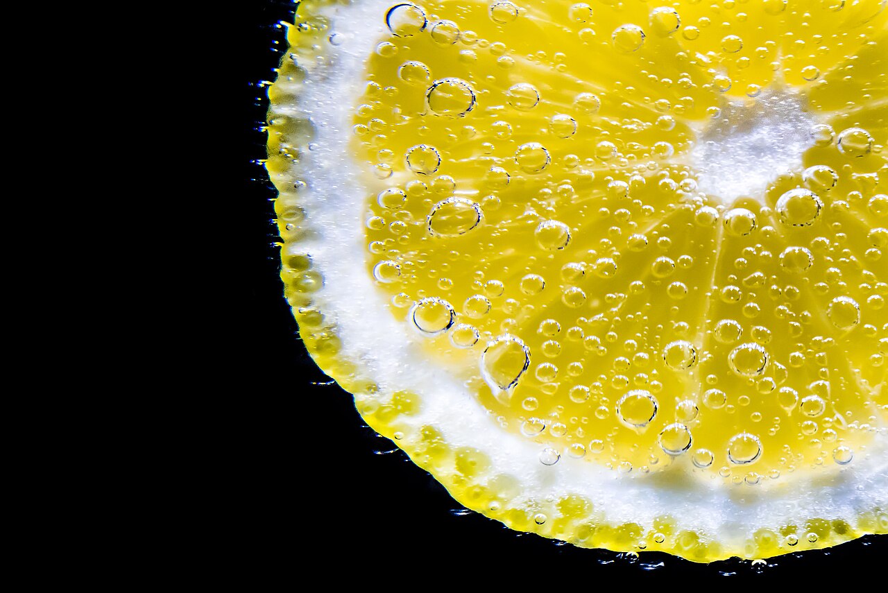A slice of lemon suspended in sparkling water, covered in bubbles